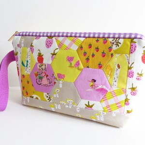 May include: A purple and yellow patchwork fabric zippered pouch with a purple strap. The pouch is made of hexagonal fabric pieces with various patterns including strawberries, birds, and a girl surfing.