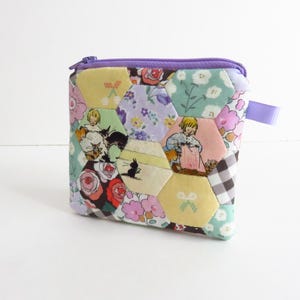 May include: A small, quilted pouch with a purple zipper and pull tab. The pouch is made of colorful, hexagonal fabric pieces with floral and storybook illustrations. The color palette includes pink, yellow, green, and purple.