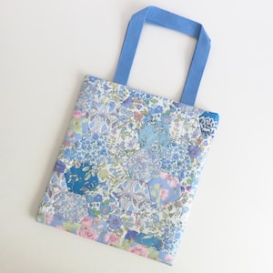 Peut inclure: Un sac fourre-tout rectangulaire présentant un motif en patchwork composé de divers tissus à fleurs dans des tons de bleu, blanc et rose. Le sac est fabriqué à partir de pièces de tissu hexagonales et possède deux anses en tissu bleu clair.