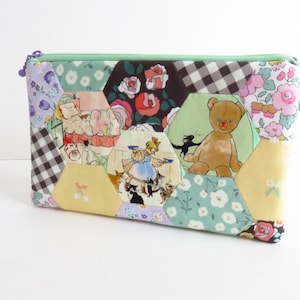 Może przedstawiać: Patchworkowa kosmetyczka z zamkiem błyskawicznym i miętowym suwakiem. Sześciokątny patchworkowy wzór zawiera kwiatowe, kratowe i ilustrowane tkaniny, w tym misia i postacie z bajek. Unikalny dodatek.