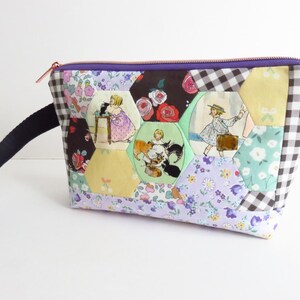 May include: A patchwork zippered pouch with a black handle. The pouch features a variety of fabrics, including floral prints, gingham, and hexagonal patches with vintage illustrations. The zipper is rose gold.