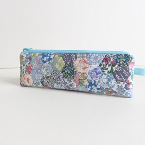 May include: A light blue zippered pencil case with a patchwork design of hexagonal floral fabric in shades of blue, pink, and green.