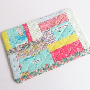 May include: A quilted patchwork item with a variety of colorful fabric squares. The design includes a bunny, floral patterns, and the text "rain rain for today". The item is a mix of pink, yellow, blue, and green.