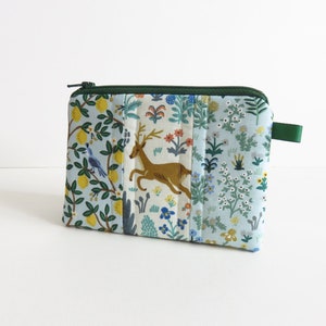 Pode incluir: Uma pequena bolsa de zíper acolchoada com fundo azul e estampa floral e animal colorida. A bolsa tem um zíper verde e uma aba de puxar verde.