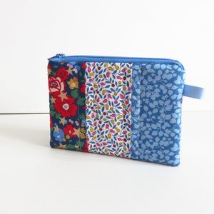 Peut inclure: Une petite pochette zippée bleue avec un motif patchwork. La pochette est composée de quatre panneaux de tissu, chacun avec un motif floral différent. Les panneaux de tissu sont cousus ensemble pour créer un design unique et coloré.