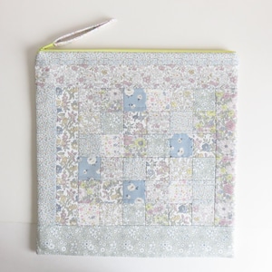 Peut inclure: Une pochette zippée en tissu patchwork bleu clair et blanc avec une fermeture éclair jaune. La pochette a un motif floral et est en coton.
