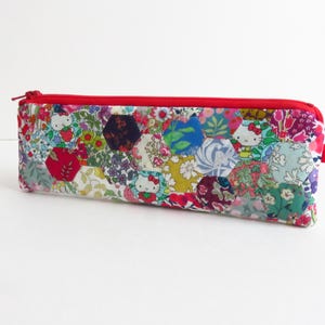 Puede incluir: Un estuche para lápices rojo con cremallera y un diseño de patchwork con una variedad de telas coloridas y un personaje de Hello Kitty.