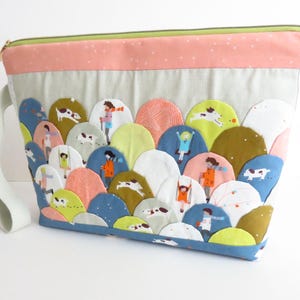 Könnte beinhalten: Eine Stofftasche mit Reißverschluss und einem geschichteten, bogenförmigen Design in verschiedenen Farben wie Blau, Grün, Rosa und Weiß. Der Stoff ist mit kleinen Illustrationen von Menschen und Hunden verziert. Sie hat eine helle Handschlaufe.