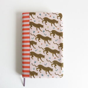 May include: A pink and orange notebook cover with a pattern of gold glitter leopards and small flowers. The cover has a red and white striped border.