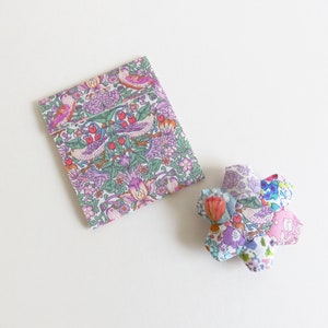 May include: A small, floral patterned fabric pouch and a matching fabric flower. The pouch is folded and the flower is lying flat on a white surface.