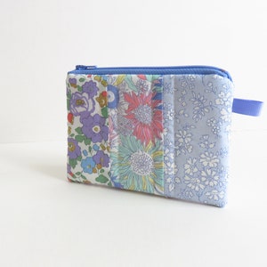 May include: A small blue zippered pouch with a patchwork design featuring floral and sunflower patterns. The pouch has a blue zipper and a blue strap.