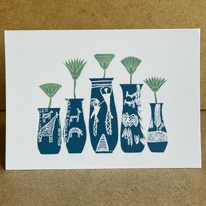 May include: A white card featuring a teal illustration of five vases with green flowers. The vases have white patterns and designs. The card is on a brown surface.