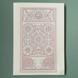 May include: A rectangular print featuring a symmetrical pattern in shades of red and light blue on a white background. The design includes floral, circular, and geometric shapes, with a spiral element at the bottom. The print is on a white paper.