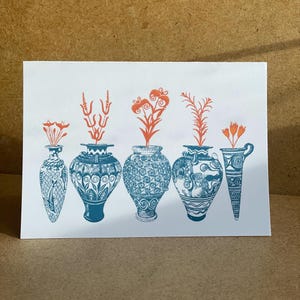May include: A white card featuring a blue and orange illustration of five decorative vases, each holding stylized orange flowers. The vases have intricate patterns and varying shapes, creating a cohesive yet diverse design.