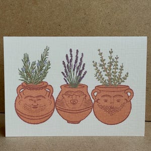 Puede incluir: Una tarjeta de felicitación con tres macetas de terracota con caras, cada una con una hierba diferente. Las hierbas incluyen romero, lavanda y otra planta verde. La tarjeta tiene un fondo texturizado blanquecino.