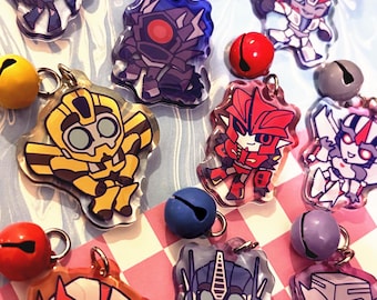 Può includere: Una collezione di portachiavi colorati con personaggi dei cartoni animati. I portachiavi presentano vari design di robot nelle tonalità di rosso, blu, giallo e viola. Ogni portachiavi ha un anello di metallo ed è abbinato a una piccola campana colorata.