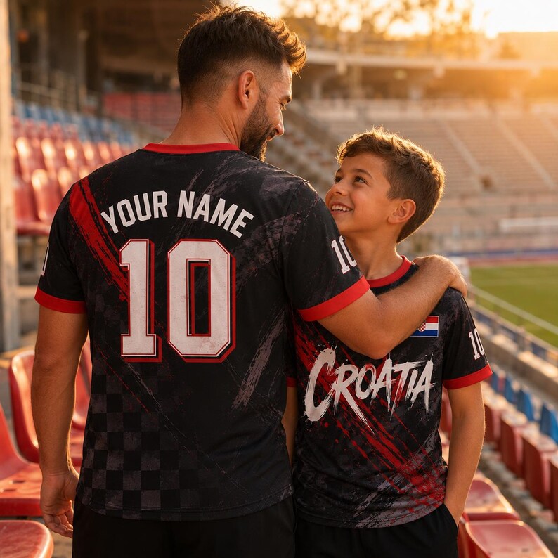 Op de afbeelding: Een zwart shirt met korte mouwen en rode accenten, voorzien van een ruitpatroon, de tekst "YOUR NAME" boven het nummer "10" op de achterkant, en de tekst "CROATIA" met een kleine Kroatische vlag op de voorkant, in een stadion.