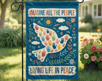 May include: A teal garden flag features the text "IMAGINE ALL THE PEOPLE" and "LIVING LIFE IN PEACE." A white dove is filled with colorful handprints. The design includes a sun, clouds, flowers, and leaves. The flag is displayed on a black metal stand.
