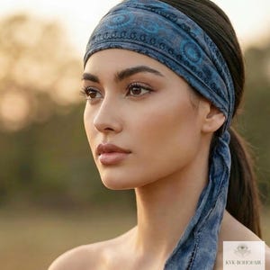 May include: A blue patterned headband with a matching tie. The headband is worn around the head and tied at the back. The design features circular and paisley-like patterns. The headband is made of a soft, possibly cotton, material.