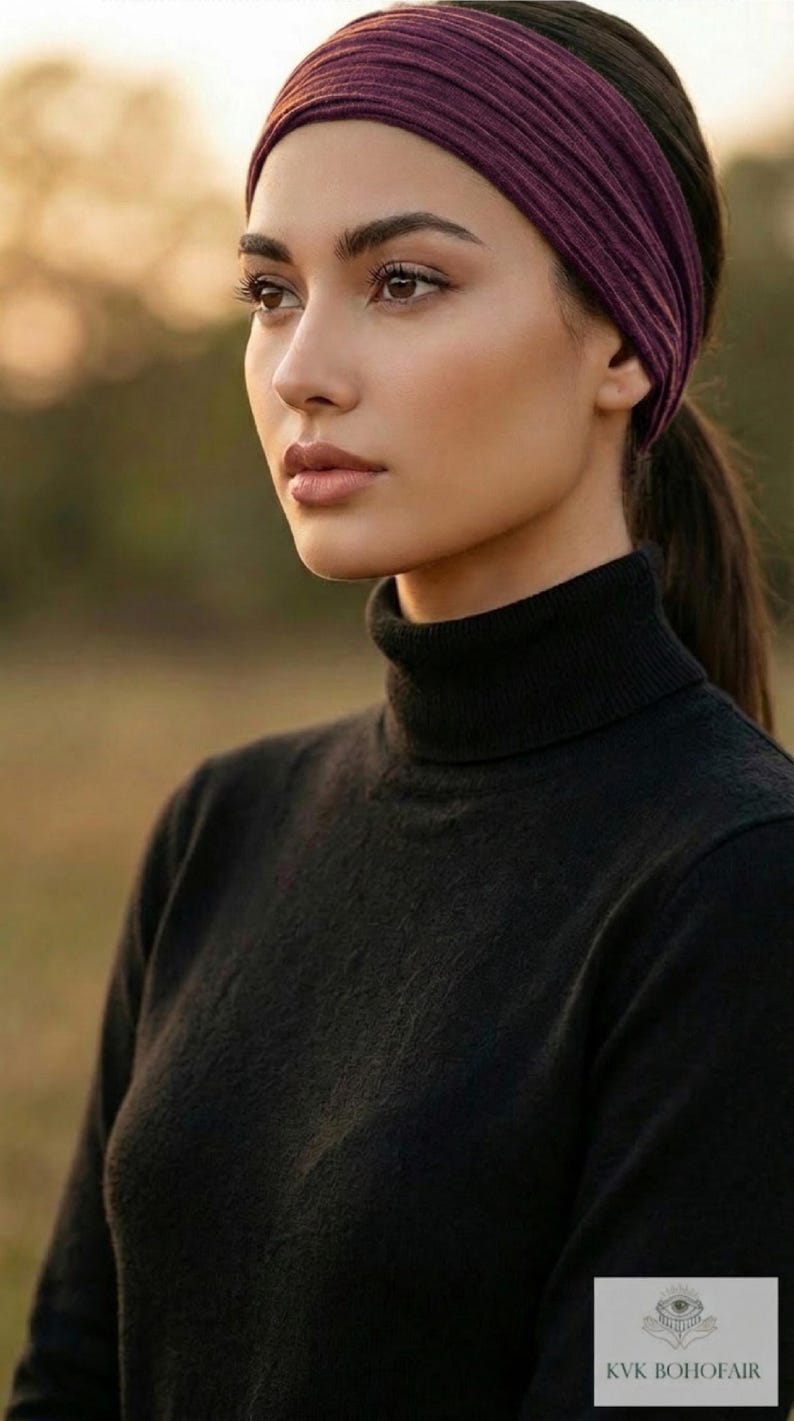 Puede incluir: Una persona con un jersey de cuello alto negro y una diadema morada oscura. La diadema es ancha y cubre la frente. El fondo est&aacute; borroso, con una luz natural suave.