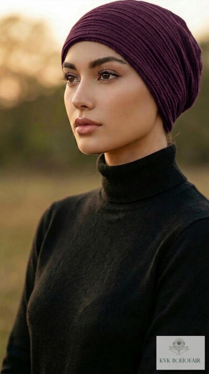 Puede incluir: Primer plano de una mujer con un gorro de punto acanalado morado oscuro y un jersey de cuello alto negro. La imagen se centra en la parte superior del cuerpo y la cara. El fondo est&aacute; borroso, con una paleta de colores c&aacute;lidos y naturales.