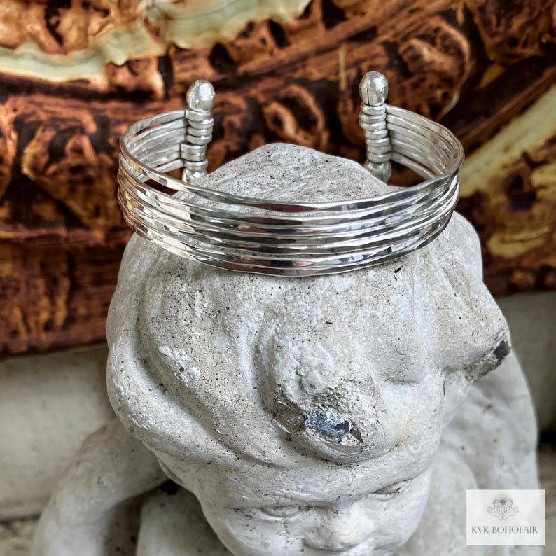May include: Silver bracelet with a hammered finish and multiple bands. The bracelet is open and has rounded ends.