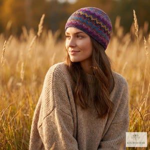 May include: A beanie hat featuring a multi-colored knit pattern with horizontal zig-zag stripes in shades of purple, blue, and gold. The hat is worn with a beige, long-sleeved, chunky knit sweater that has a ribbed neckline and loose fit.