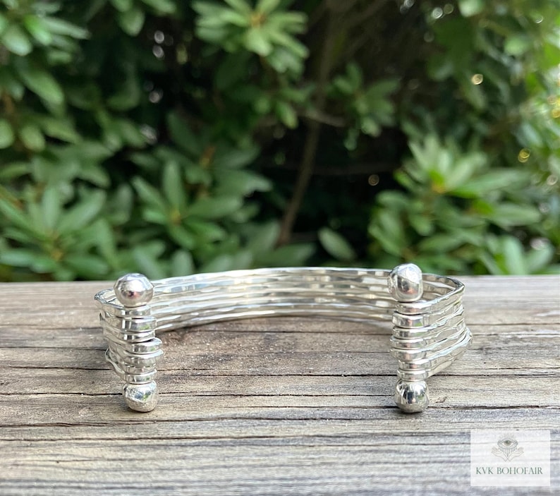 May include: A silver bangle bracelet with a hammered finish and rounded ends. The bracelet is made of multiple strands of wire that are woven together.