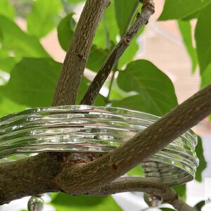 May include: A silver bracelet with a hammered texture. The bracelet is made of multiple bands stacked on top of each other. The bracelet is resting on a tree branch.