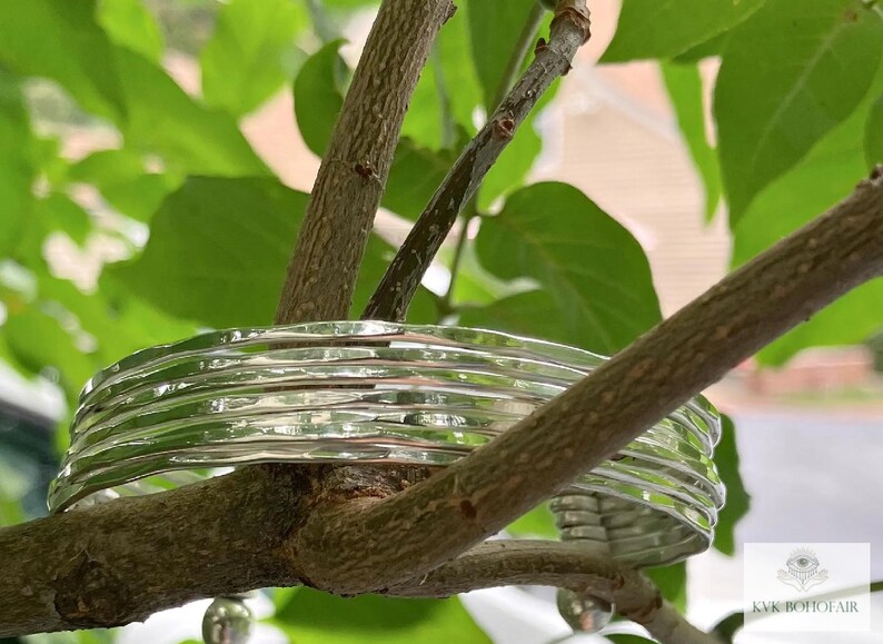 May include: A silver bracelet with a hammered texture. The bracelet is made of multiple bands stacked on top of each other. The bracelet is resting on a tree branch.