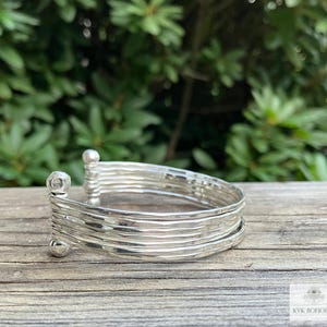 May include: Silver bangle bracelet with a hammered finish. The bracelet is made of multiple thin bands stacked together.