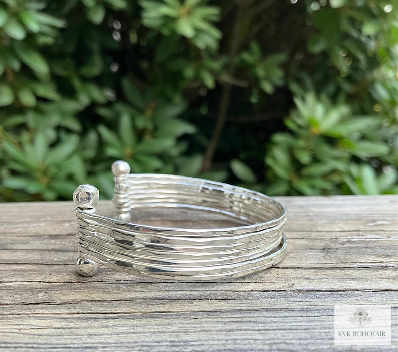 May include: Silver bangle bracelet with a hammered finish. The bracelet is made of multiple thin bands stacked together.