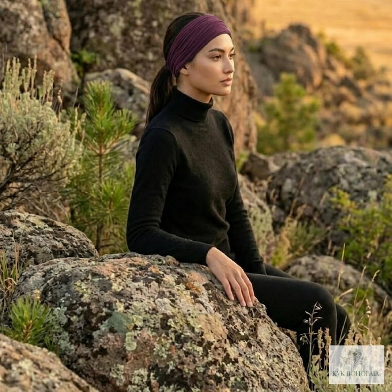 Puede incluir: Una mujer con un cuello alto y leggings negros, con una diadema morada oscura. Est&aacute; sentada en una gran roca, con un fondo natural de rocas y vegetaci&oacute;n. La diadema es de color s&oacute;lido.