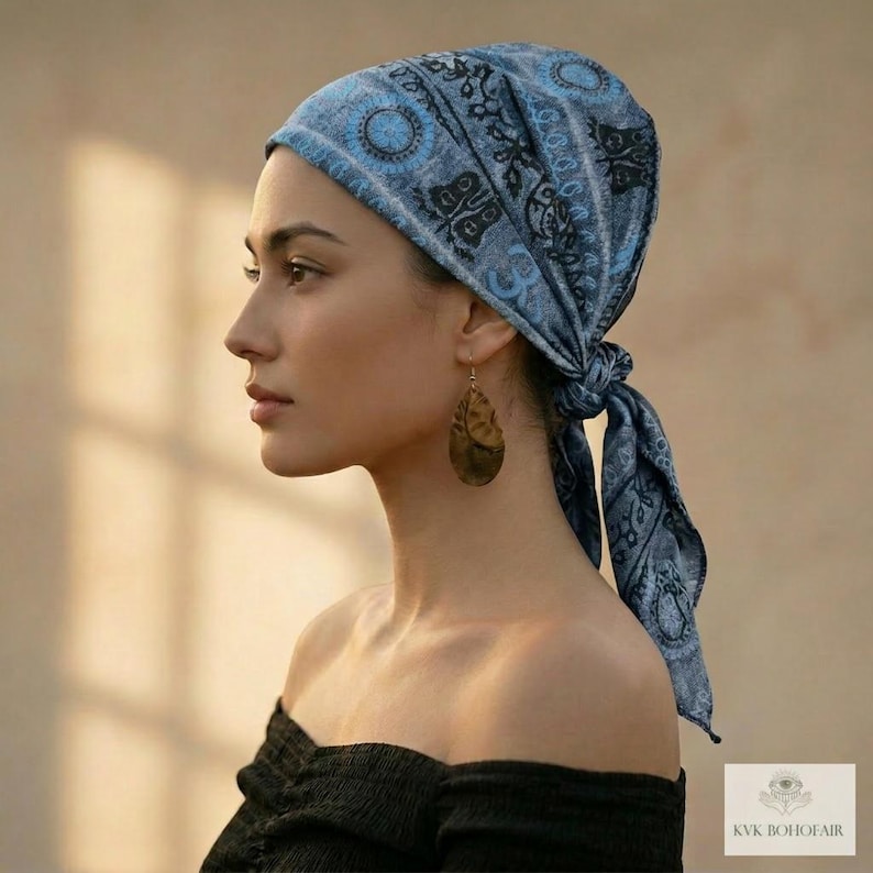 May include: A light blue headscarf with a paisley design and a knot at the back. The headscarf is worn with a black off-the-shoulder top and gold-colored teardrop earrings. The image is a side profile of a person.