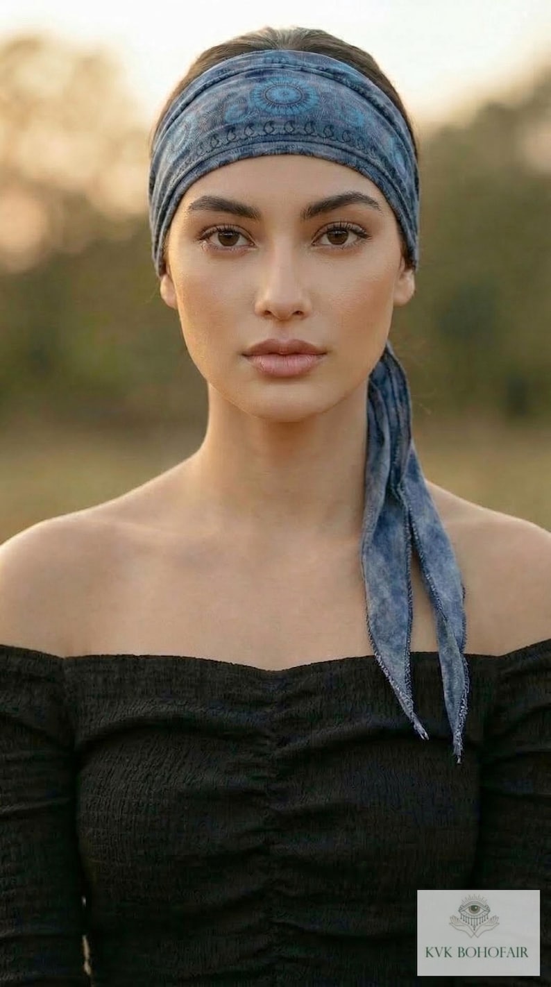 May include: A woman wearing a blue patterned headband and a black off-the-shoulder top. The headband matches the scarf-like ties hanging down the back. The image is set against a blurred outdoor background. The text "KVK BOHOFAIR" is in the bottom right corner.
