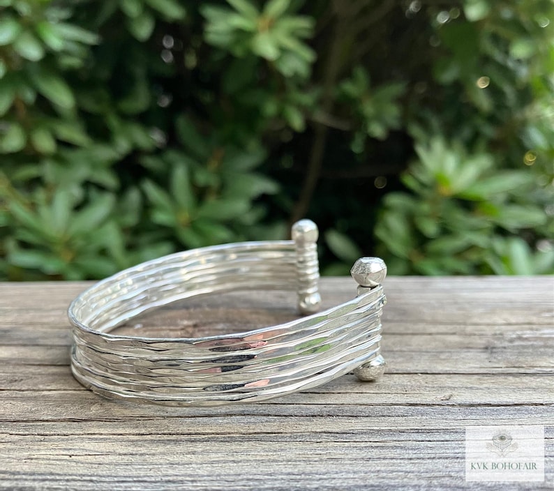 May include: A silver bracelet with a hammered texture and multiple bands. The bracelet has rounded ends.