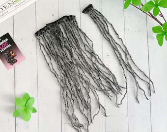 May include: Two bundles of gray dreadlock extensions are displayed on a white wooden surface. One bundle is a full weft, and the other is a single strand. A small card with the text "Premium Loc Designs" and a woman's profile is visible.