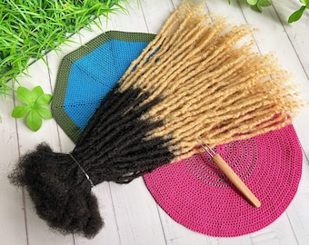 May include: A set of two-tone synthetic dreadlocks in black and blonde. The dreadlocks are displayed on a pink crocheted surface with a wooden crochet hook.