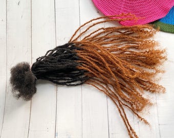 May include: A bundle of brown and black ombre synthetic dreadlocks. The dreadlocks are long and straight with a slight curl at the ends.