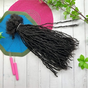 May include: Black synthetic dreadlocks hair extensions on a blue and green crocheted mat. Two pink crochet hooks are on the white wooden surface.