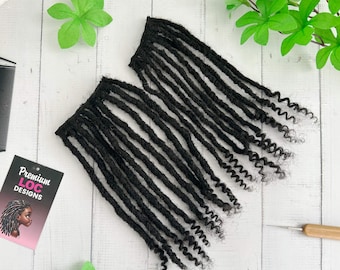 May include: Two bundles of black dreadlocks with curly ends are displayed on a white wooden surface. The dreadlocks are arranged in a neat, parallel fashion. A small card with the text "Premium LOC DESIGNS" and an illustration of a person with dreadlocks is visible.