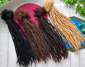 May include: Four sets of synthetic dreadlocks in black, brown, light brown, and blonde. The dreadlocks are arranged in a row on a white wooden surface.