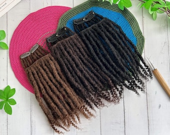 May include: Three sets of dreadlock extensions in shades of brown and black, each with a clip for easy attachment. The extensions are arranged on a white wooden surface, with a pink, blue, and green crocheted circle in the background.