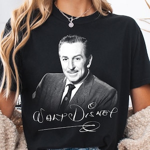 May include: Black t-shirt featuring a black and white portrait of Walt Disney. The shirt has the name "Walt Disney" in a white script font. The shirt is a classic crew neck style.