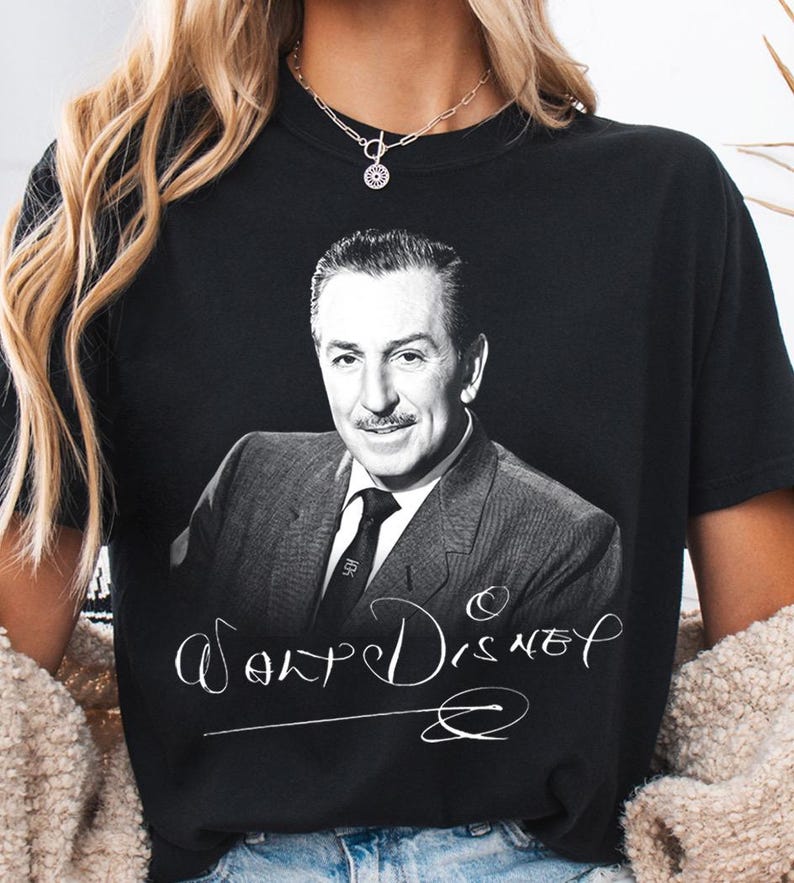 May include: Black t-shirt featuring a black and white portrait of Walt Disney. The shirt has the name "Walt Disney" in a white script font. The shirt is a classic crew neck style.