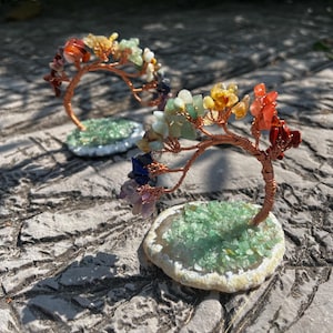 May include: Two small wire-wrapped trees with colorful gemstones, each on a green agate base. The trees are bent into an arc shape.