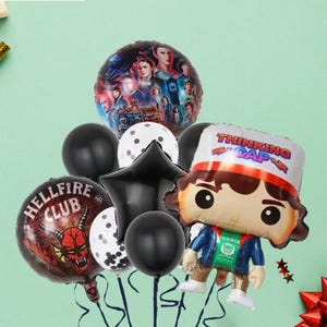 May include: A set of balloons, including a large foil balloon with a group of people, a black star-shaped balloon, and several round black and white polka dot balloons. One balloon features a cartoon character with the text "THINKING CAP". The text "Set A" is also visible.