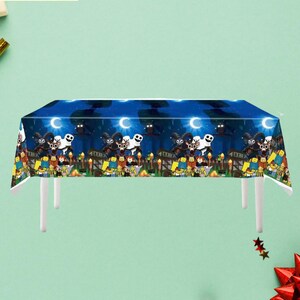 May include: A blue tablecloth with a Halloween-themed design featuring cartoon characters, bats, and moons. The tablecloth measures 54 x 108 inches. The image also includes the text "Tablecloth" and the dimensions in centimeters.