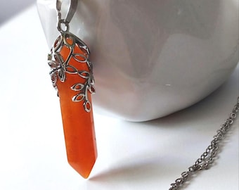 Puede incluir: Collar plateado con un colgante de cristal naranja. El colgante está engastado en un marco decorativo plateado con detalles de hojas. La cadena del collar también es plateada. El colgante mide unos 5 cm de largo.
