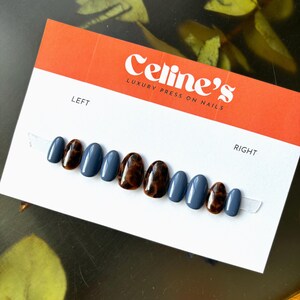May include: A set of press-on nails in a variety of shapes and colors. The nails alternate between a solid blue-gray and a tortoiseshell pattern. The card reads "Celine's Luxury Press On Nails."